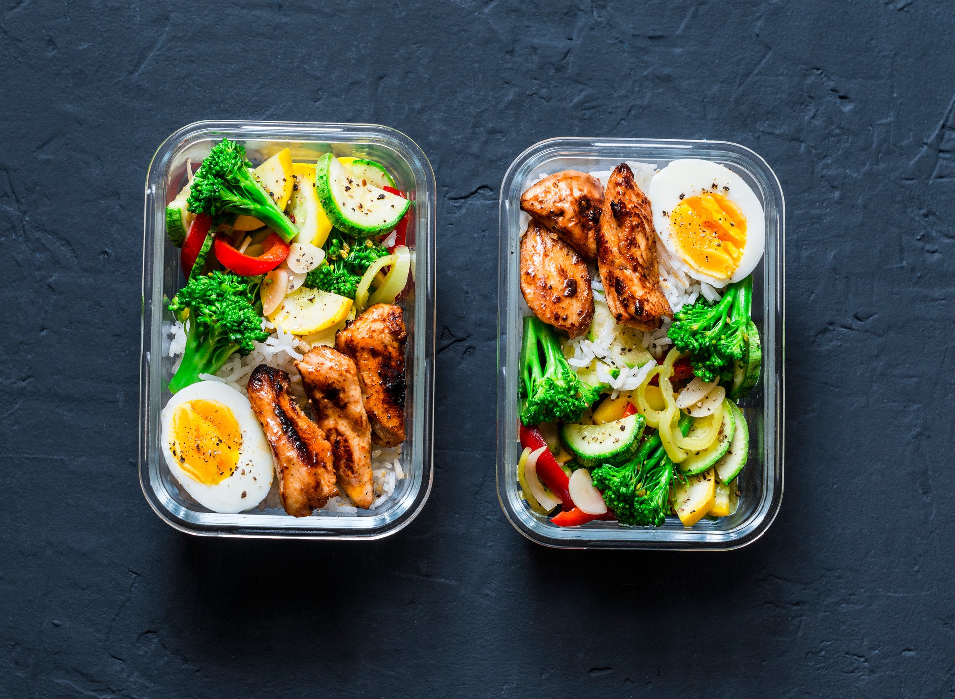 Rice, stewed vegetables, egg, teriyaki chicken - healthy balanced lunch box on a dark background, top view. Home food for office concept